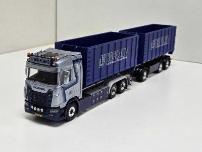 Scale-model Scania truck pulling two blue Hoffland container trailers on a white surface with minimal background.