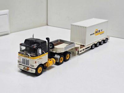 Small-scale toy truck and trailer set with a white shipping container marked van der Herik, on a white surface in a studio.