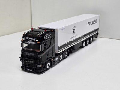 Black Scania truck with a long white trailer featuring 'Poplawski' branding and a '30 years'/Delivering Quality slogan, photographed from the front-left.