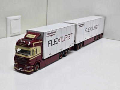 Red Scania toy truck with three white trailers labeled FLEXILAST, photographed from the front-left side on a white surface.