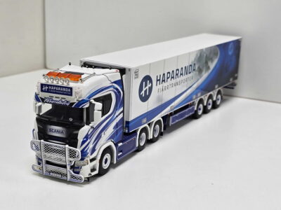 Scale model of a white and blue Haparanda freight truck with a long trailer displaying branding on a white surface
