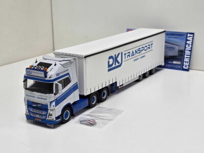20260523_163213 - Degen Miniaturen Scale model white DK Transport truck with blue accents and a long trailer, set on a white surface with a blue, boxed logo in the background (text reads DK Transport Europe–Norway).