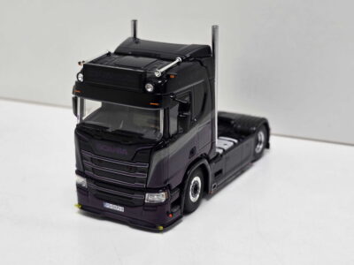 Black toy Scania truck model with chrome exhausts and detailed front grille on a light background, angled slightly to show the cab.