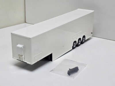 White multi-axle semi-trailer model on a white surface, with a small clear bag containing gray parts nearby.