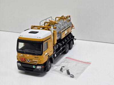 20260819_131647 - Degen Miniaturen Die-cast yellow and black construction truck model with a gray crane and orange rails on a white surface, viewed from the front-left.