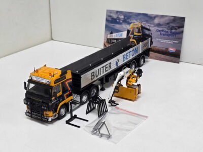 Toy concrete mixer trucks on a white surface, yellow cabs and silver trailers with 'BUTER BETON' lettering; a promotional image in the background.