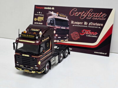 Two detailed Scania toy trucks on a white surface with a Tekno Collectables display in the background.