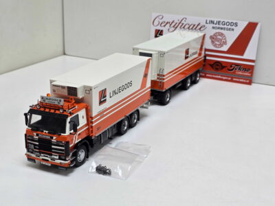 Scale model orange and white Linjegods semi-truck with trailer on a white surface; backdrop shows 'Certificate' and Linjegods branding.