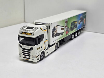 Scale-model white Scania truck with a long colorful trailer, shown from the front-left in a studio setting.