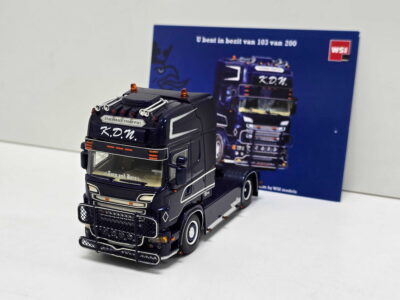 Black toy truck with orange beacon lights and chrome accents, labeled K.D.N., on a white surface with a blue truck image box in the background.