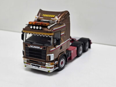 Brown toy Scania truck model with chrome detailing and a light bar on the roof, set against a white background.