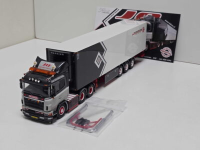 20260919_144957 - Degen Miniaturen Scale model Scania truck with a white-and-black trailer on a white surface, packaging in the background, and a clear plastic bag of accessories nearby.