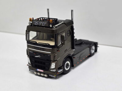 Scale model of a dark gray Volvo truck with a detachable trailer, detailed cab, chrome exhausts, and orange warning lights on top