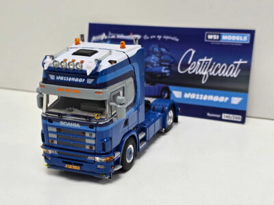 Front view of a blue Scania model truck with chrome grille and orange lights, set on a white surface with a certificate box in the background.