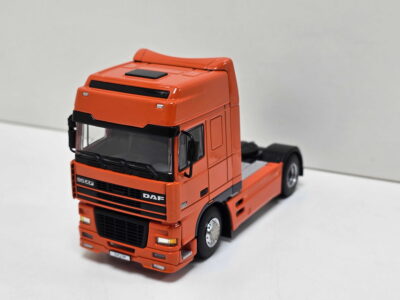 Orange toy truck cab with detailed grille and windshield on a white background, front view from the left side