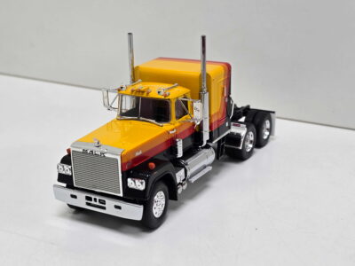 Close-up of a yellow and orange toy semi-truck model with chrome front grille and exhaust stacks, viewed from the front-left angle.