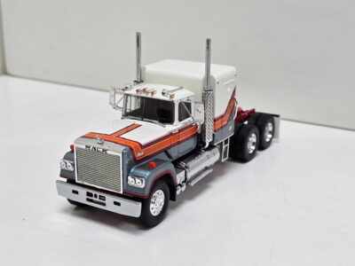 White and orange scale-model Mack truck with chrome exhaust stacks, photographed from the front-left.