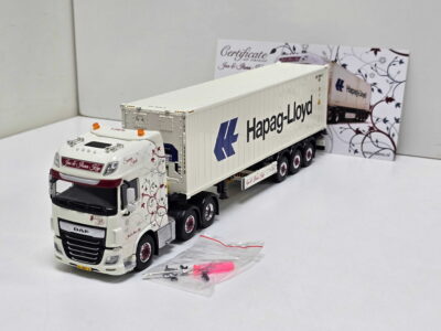 Scale-model white DAF truck with floral decals pulling a Hapag-Lloyd container in a studio setup, backdrop with decorative pattern.
